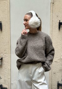Pull en maille marron à poils avec des poignets côtelés, assorti à un pantalon crème taille haute. Des cache-oreilles en fausse fourrure blanche complètent le look.
