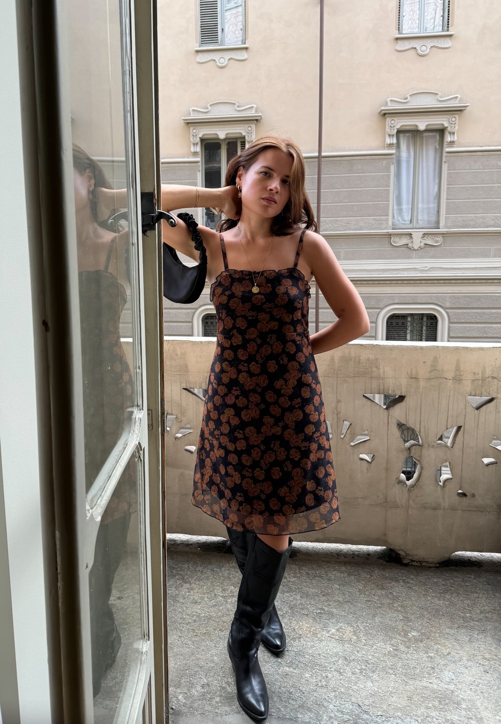 Μαύρο floral φόρεμα με διάφανη υφή, διακοσμημένο με καφέ ροζ σχέδια, λεπτές τιράντες και άνετη γραμμή, συνδυασμένο με μαύρες μπότες έως το γόνατο.