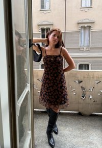 Μαύρο floral φόρεμα με διάφανη υφή, διακοσμημένο με καφέ ροζ σχέδια, λεπτές τιράντες και άνετη γραμμή, συνδυασμένο με μαύρες μπότες έως το γόνατο.