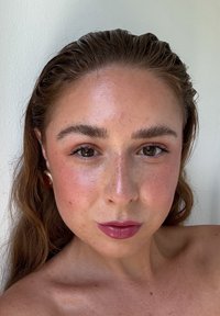 Nærbilde av et ansikt med middels hudtoner, langt brunt hår, lett sminke og dype rosa lepper; if ørt sirkulære gulløredobber.