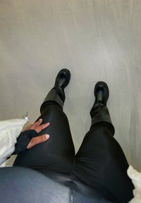 Botas de borracha pretas para o tornozelo com solas grossas, combinadas com leggings pretas justas. As botas apresentam uma textura suave e um leve alargamento no tornozelo.