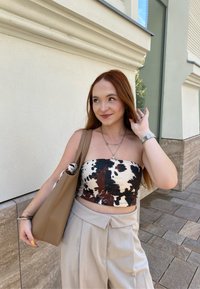 Top corto a stampa marrone e crema, pantaloni beige a vita alta e una borsa a tracolla color sabbia. Gli accessori includono collane a strati e un orologio.