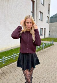 Cardigan bordeaux avec un col arrondi et une fermeture à boutons, associé à une jupe noire à volants et des leggings à motif de dentelle.