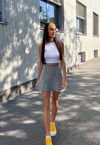 Γκρι φαρδύ σορτς, λευκό κομμένο μπλουζάκι και φωτεινές κίτρινες αθλητικές παπούτσια. Μακριά μαλλιά χτενισμένα με μια κίτρινη κορδέλα. Αστική φόντο με παράθυρα.