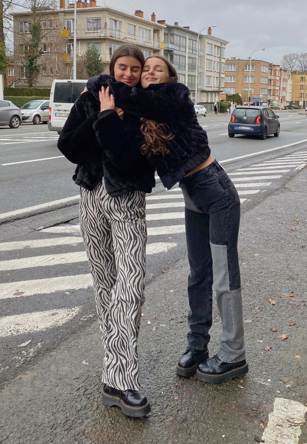 Chaqueta de piel sintética negra, pantalones de pierna ancha con estampado de cebra y vaqueros oscurecidos con parches claros. Zapatos de plataforma negros y gruesos. Entorno urbano.