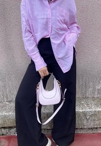 Ριγέ ροζ πουκάμισο με κουμπιά, μαύρο παντελόνι σε φαρδιά γραμμή και μια μικρή ανοιχτή ροζ τσάντα με χρυσές λεπτομέρειες και ρυθμιζόμενο λουράκι.