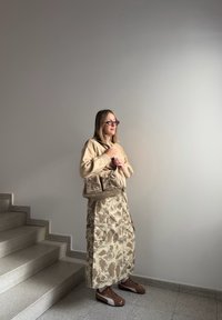 Suéter de malha bege, saia com padrão de camuflagem, sapatilhas desportivas castanhas e uma bolsa taupe com três bolsos. Cores neutras e design em camadas.