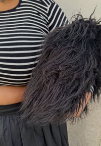 Accessoire en fourrure noire duveteuse avec des mèches longues et texturées. Stylisé avec un haut court rayé noir et blanc, assorti à une jupe noire.