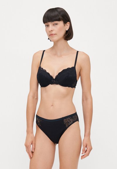 Sostén de encaje negro con copas moldeadas, tirantes delgados y un detalle de lazo en el centro. Parte inferior de bikini negra con acentos de encaje en los lados.