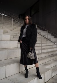 Casaco de pêlo sintético preto, blusa de lantejoulas prateadas, saia preta de cetim, meias pretas até ao tornozelo e bolsa de contas prateadas na escadaria.