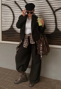Fekete blézer fehér felső felett, deréknál megkötött kockás ing, fekete bő szárú nadrág, barna laza csizma és barna velúr táska. Kiegészítők között napszemüveg is van.