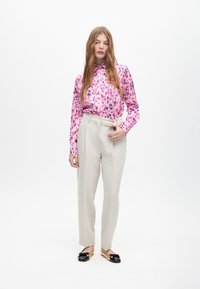 Blusa con stampa leopardata in tonalità rosa, pantaloni beige a vita alta e mocassini neri con dettagli dorati. Texture morbide in tutto l'outfit.