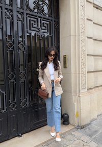 Blazer en lin beige sur une chemise blanche, jeans droit bleu clair, talons pointus blancs et une pochette marron. Des lunettes de soleil noires complètent le look.