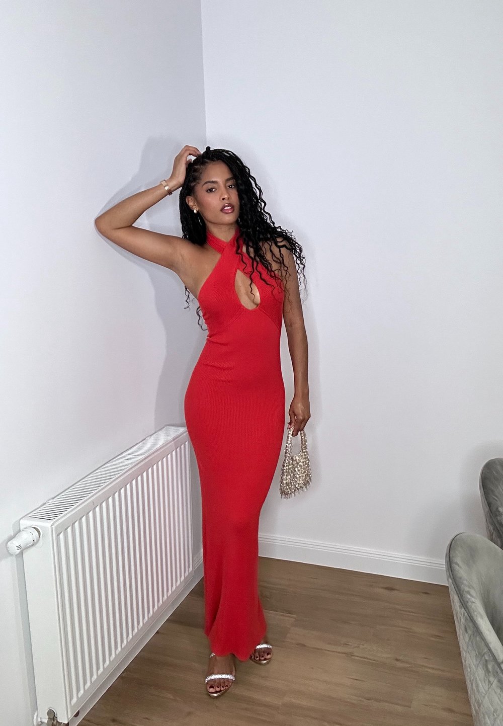 Vestido maxi rojo con trenzado y escote halter, y corte en forma de llave. El conjunto se acompaña de sandalias plateadas de tiras y un bolso de cuentas.