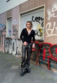 Μαύρος πουλόβερ με κουμπιά και βαθύ V-λαιμό, και φαρδιά μαύρα δερμάτινα παντελόνια. Χοντρά μαύρα παπούτσια και στρωματοποιημένα ασημένια κοσμήματα συμπληρώνουν την εμφάνιση.