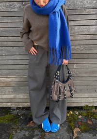 Brun sweater, blå frynset tørklæde, grå stribede bukser med vide ben, blå sneakers og en brun håndtaske med sorte detaljer og sølvhardware.