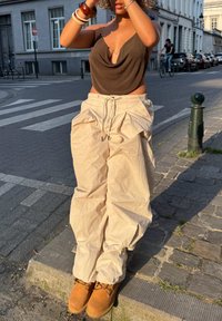 Beige, losse cargo-broeken, een bruine tanktop en bruine laarzen. De stof heeft een gekreukte textuur met een trekkoord in de taille en zijzakken.