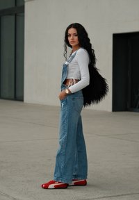 Pantalones de mezclilla azul con una camisa blanca de manga larga recortada, zapatos rojos y un bolso negro de pelaje. Destaca el lazo en la camisa.