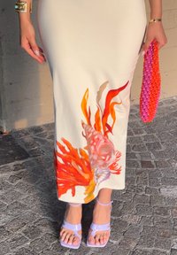 Vestido midi blanco con motivos coloridos de corales y peces en el dobladillo. Llevado con sandalias de tiras lavanda y un clutch de mimbre rosa.