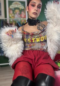 Gesneden rode short met een grafisch ontwerp, een meerkleurig patroon top met de tekst "WESTWOOD" en een pluizige witte bontsjaal. Zwarte knielaarzen.