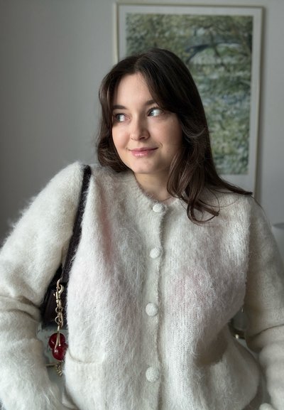 Cardigan blanco y esponjoso con escote redondo, con tres botones y bolsillos. Combinado con una correa oscura y un bolso encantador rojo.