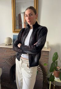 Črno in sivo vzorčasta jakna na zadrgo z visokim ovratnikom, narejena iz mehkega puhasto materiala. Kombinirana s svetlo bež hlačami.