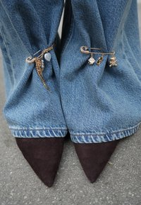 Jean en denim à coupe ample, avec des accents et des breloques en métal doré, associé à des talons pointus en daim brun foncé.