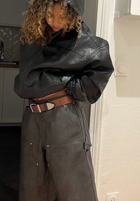 Čierna kožená veľkoplošná mikina s textúrovaným povrchom, v páre s tmavými koženými nohavicami s veľkými vreckami a hnedým opaskom so striebornou prackou.