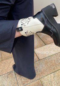 Bota de tornozelo em couro preto e branco com embossing floral, design contornado e salto bloco grosso. Acentos de costura realçam o padrão.