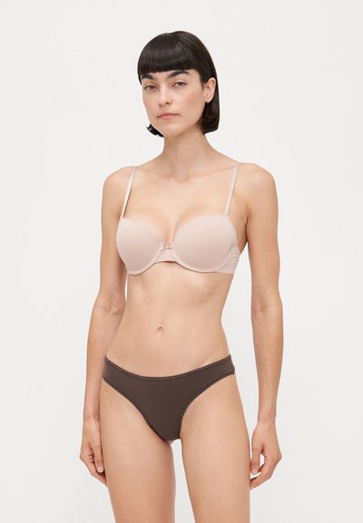 Sujetador moldeado beige con tirantes finos y un detalle de lazo en el centro, combinado con una parte inferior de bikini marrón oscuro, que presenta una tela suave y elástica.