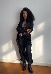 Un sacou negru peste un bralet metalic, asortat cu pantaloni largi negri și botine. O eșarfă neagră cu franjuri completează ținuta.