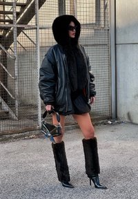 Črna usnjena prevelika jakna z umetnim krznom, črna mini krila, škornji do kolen iz umetnega krzna ter majhna črna torbica s strukturirano zasnovo.