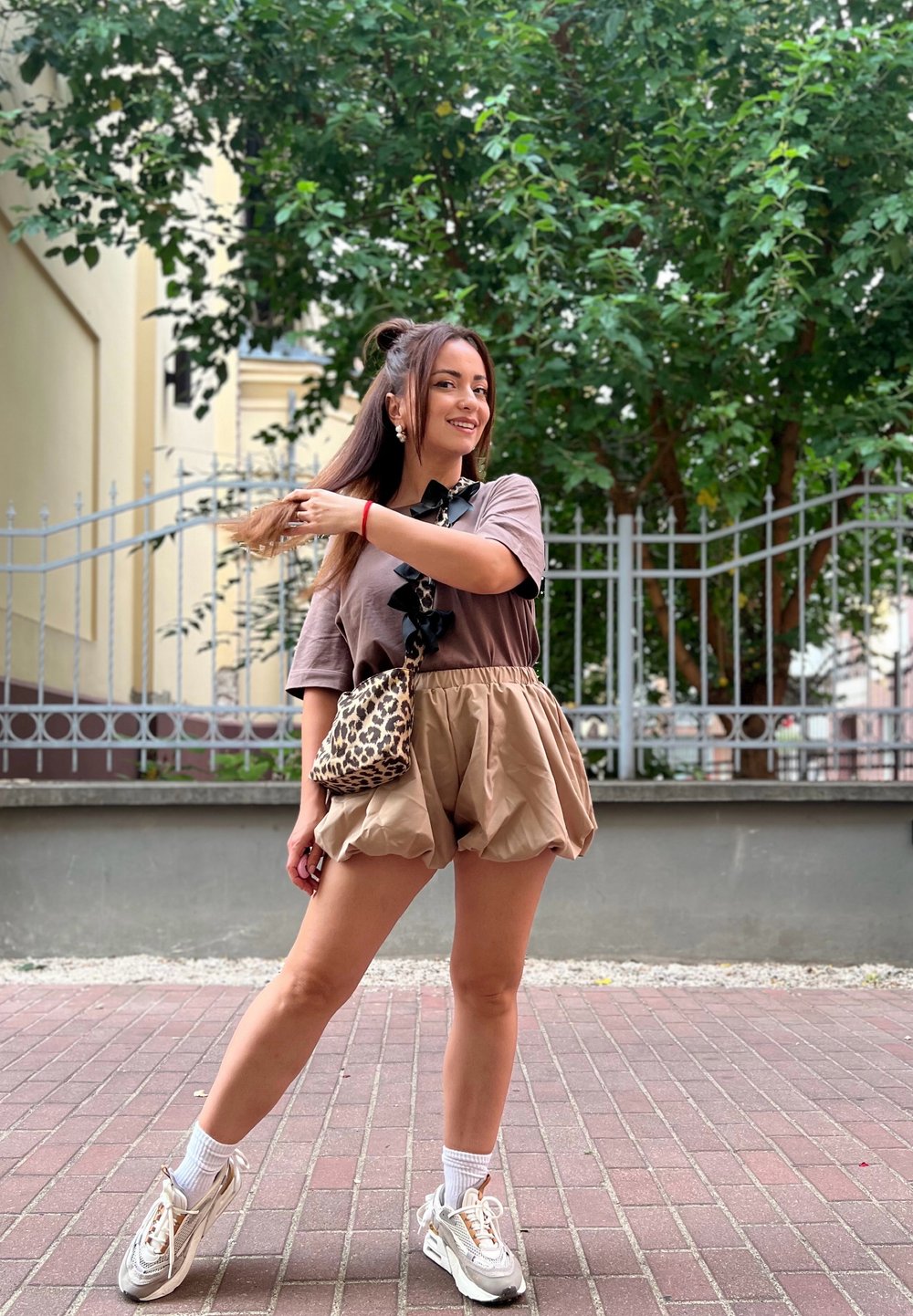 Μπεζ σορτσάκια με βολάν στο τελείωμα, σε συνδυασμό με καφέ μπλούζα με βολάν στον λαιμό. Τα αξεσουάρ περιλαμβάνουν τσάντα με λεοπάρ σχέδιο και αθλητικά παπούτσια.