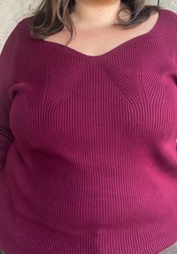 Bordový rebrovaný pletený sveter s výstrihom do V, so štruktúrovanými diagonálnymi švami na prednej strane a voľným strihom.