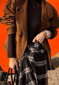 Hnedá semišová dvojradová bunda s vyhrnutými rukávmi, skombinovaná s čiernym rolákom a károvanou sukňou v tmavých tónoch. Akcent v podobe čiernej kabelky.