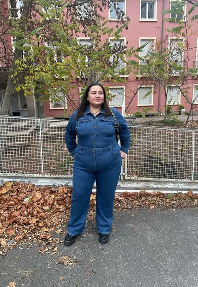 Mono de denim en azul oscuro con cierre de botones, mangas largas, dos bolsillos en el pecho y corte holgado; combinado con zapatos negros y un bolso de cadena.