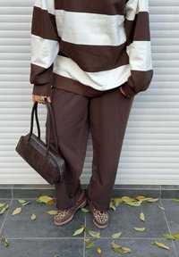 Ylisuuri ruskeavalkoraidallinen collegepaita, ruskeat housut, leopardi-kuosiset kengät ja tummanruskea käsilaukku, asetettuna liuskekivilaatoille lehtien kanssa.