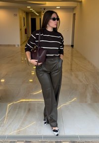 Pull noir en tricot avec des rayures blanches, pantalon en similicuir vert olive taille haute, chaussures noires et blanches à motif et un sac à main bordeaux.