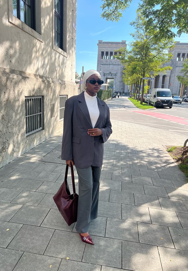 Grijze oversized blazer, witte coltrui, wijde grijze broek, bordeaux handtas en bordeaux puntige schoenen. Zonnebril gedragen.
