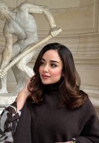 Μοντέλο που φοράει ένα σκούρο καφέ poncho με ψηλό λαιμό, με απαλή υφή, διαθέτοντας φωτεινά, ανάγλυφα μανίκια, μπροστά από ένα μαρμάρινο άγαλμα.