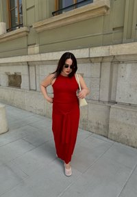 Robe rouge, ajustée, sans manches avec un détail à nouer à la taille ; associée à des chaussures blanches et un léger sac à épaule. Texture de tissu lisse.