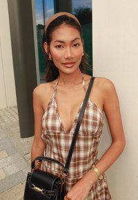 Brun og beige plaid halterneck kjole med en dyb udskæring; parret med en sort håndtaske med gyldne accenter og et tekstureret guldarmbånd.