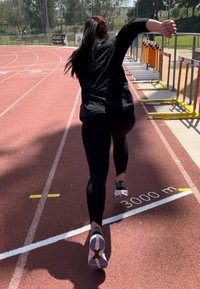 A runner in black athletic gear strides purposefully along a red track, eyes fixed ahead. The track features a clearly visible 3000 metre marker.