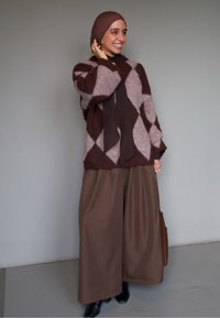 Cardigan tricotat cu model argyle maro și roz peste o bluză maro închis și pantaloni maro cu croială largă. Geantă maro și pantofi negri.