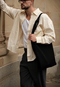 Gestreifte creamfarbene und beige Button-up-Bluse über einem weißen T-Shirt, kombiniert mit dunklen Hosen und einer schwarzen Schultertasche. Strukturiert Stoffe.