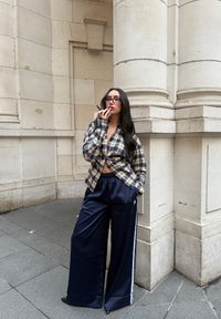 Koszula na guziki w kratę w kolorze beżowym i granatowym, o krótkim kroju. Luźne granatowe spodnie dresowe z białymi bocznymi paskami i logo Adidas.