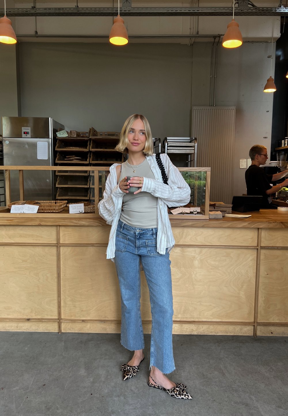 Ljus träfärgad disk i ett kafé med en person som bär en randig oversized skjorta, en beige linne och utsvängda jeans med rå fåll.