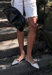 Fehér, hegyes orrú lapos cipők, hátragorítós dizájnnal és vékony pántokkal, kopott fehér sortokkal és fekete bőr táskával párosítva.