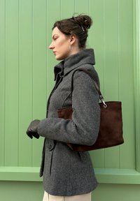 Manteau gris en mélange de laine avec col montant, sac à main en daim marron et gants en cuir noir sur un fond vert clair.