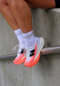 Jalad, millel on valged sokid ja valge-oranžid jooksujalatsid, toetuvad metallist rööpa vastu betoonseina.